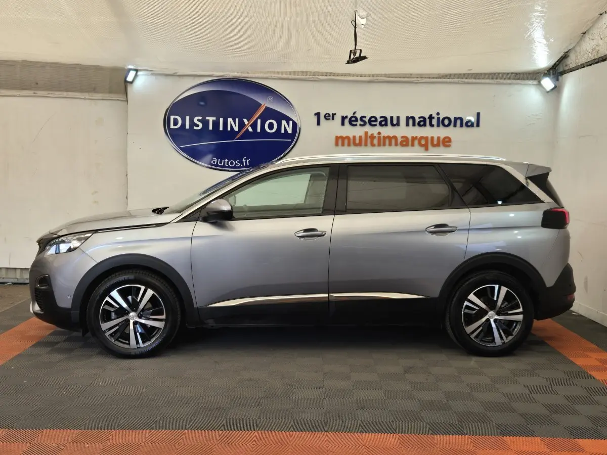 Peugeot 5008 gris clair vue de profil côté gauche, avec jantes alliage et toit chromé en intérieur showroom.