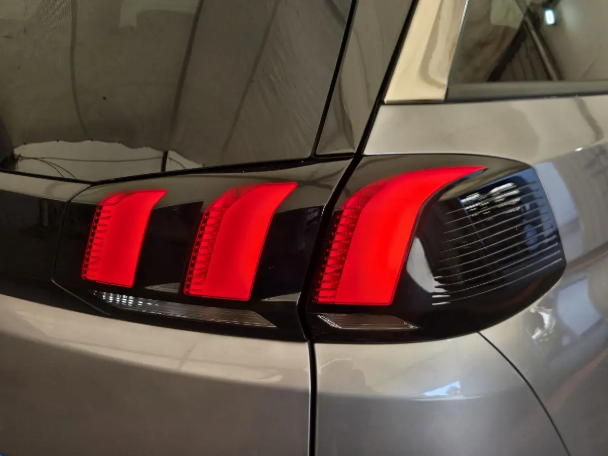 Gros plan sur le feu arrière droit rouge vif d’un Peugeot 5008 gris clair, soulignant ses lignes modernes.