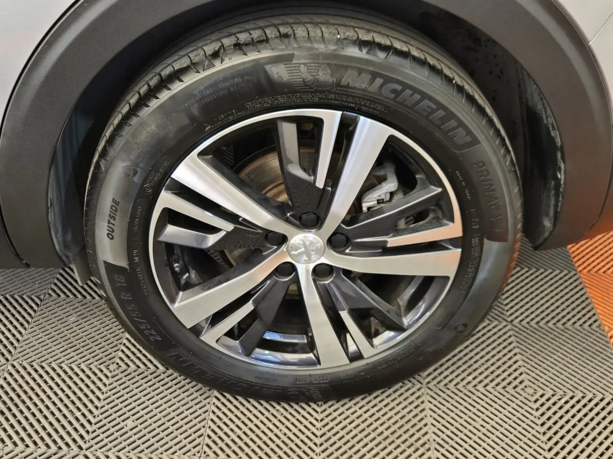 Gros plan sur la roue avant droite du Peugeot 5008 gris clair, mettant en valeur la jante alliage bicolore et le pneu Michelin.