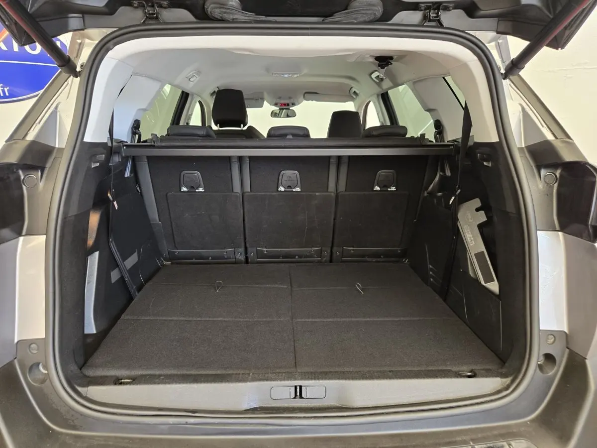 Coffre ouvert vu de l'arrière d'un Peugeot 5008 gris clair avec banquette arrière partiellement rabattue.