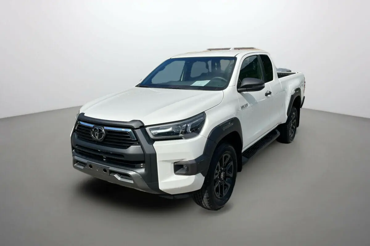 Toyota Hilux 4x4 blanc pur en vue 3/4 avant droit, avec calandre noire et jantes foncées distinctives.
