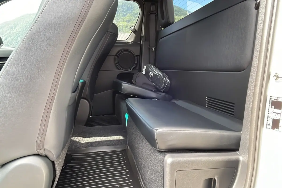 Vue intérieure arrière côté droit du Toyota Hilux 2025 X-TRA D-4D blanc avec banquette rabattable et siège avant en cuir noir.