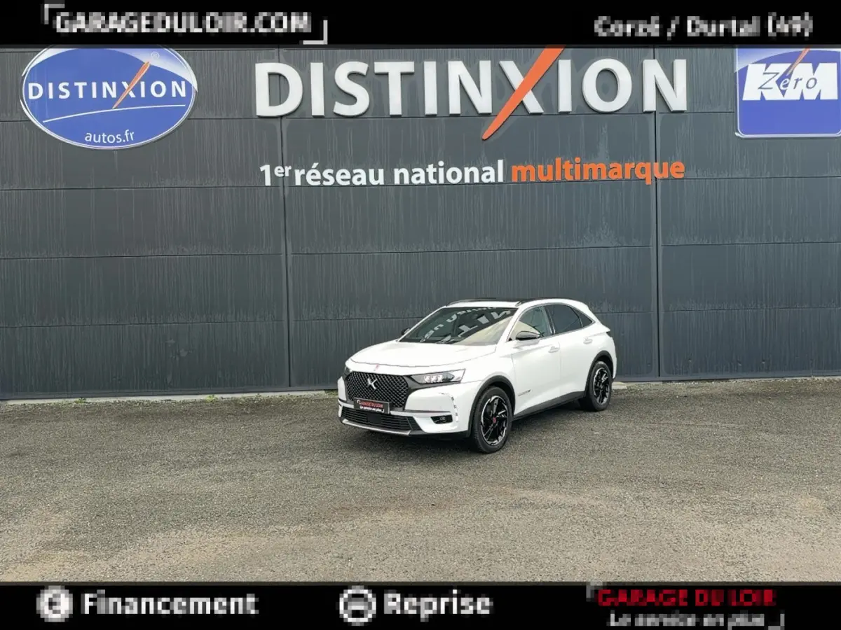 DS7 Crossback blanc en 3/4 avant droit, avec calandre noire et jantes noires, devant un mur gris marqué Distinxion