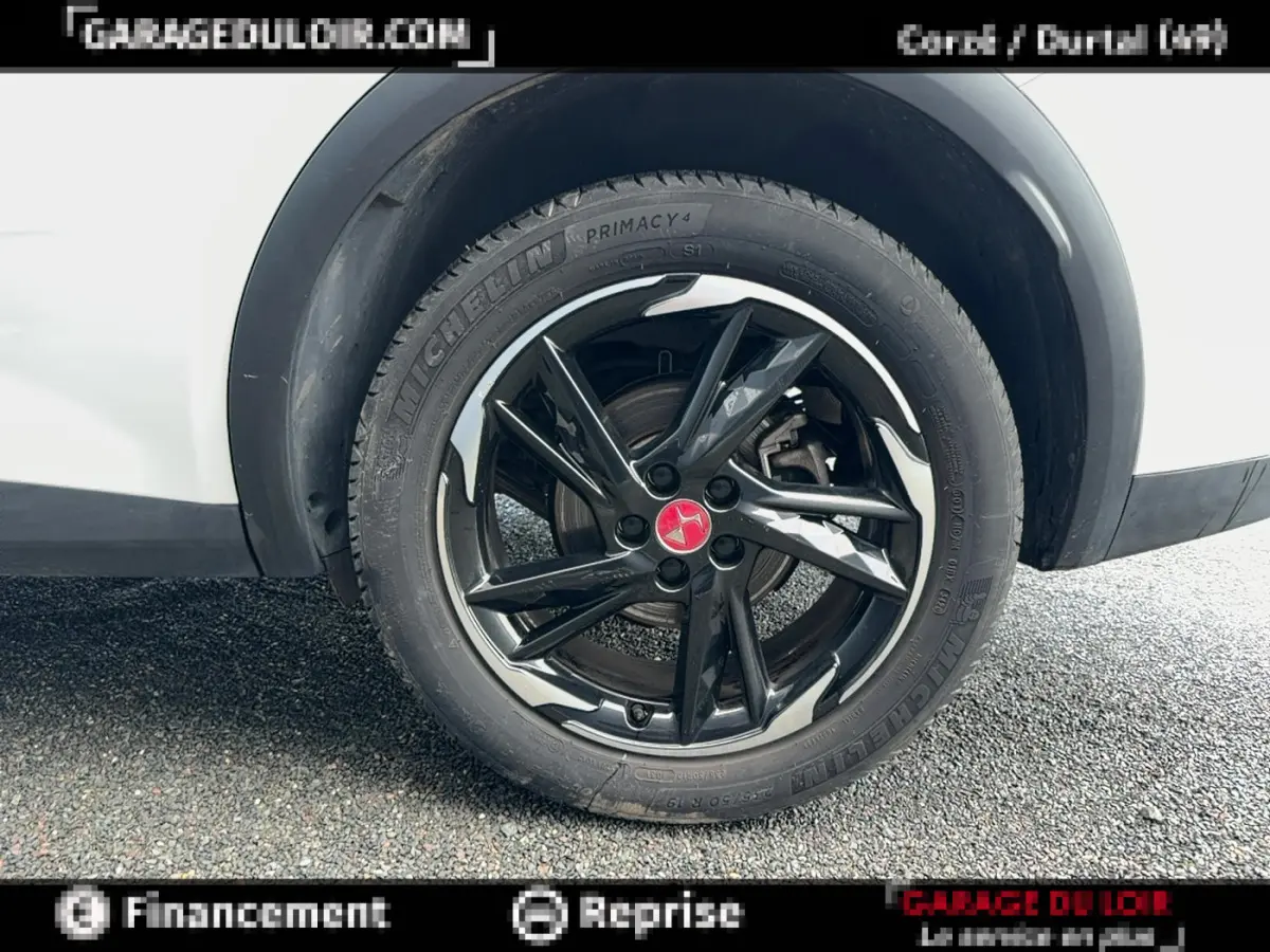 Gros plan sur la roue arrière droite avec jante noire brillante et logo rouge sur DS7 Crossback blanc.