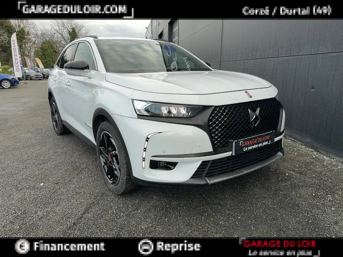 Vue 3/4 avant droite du DS7 Crossback blanc avec calandre noire et jantes noires, stationné devant un mur gris.
