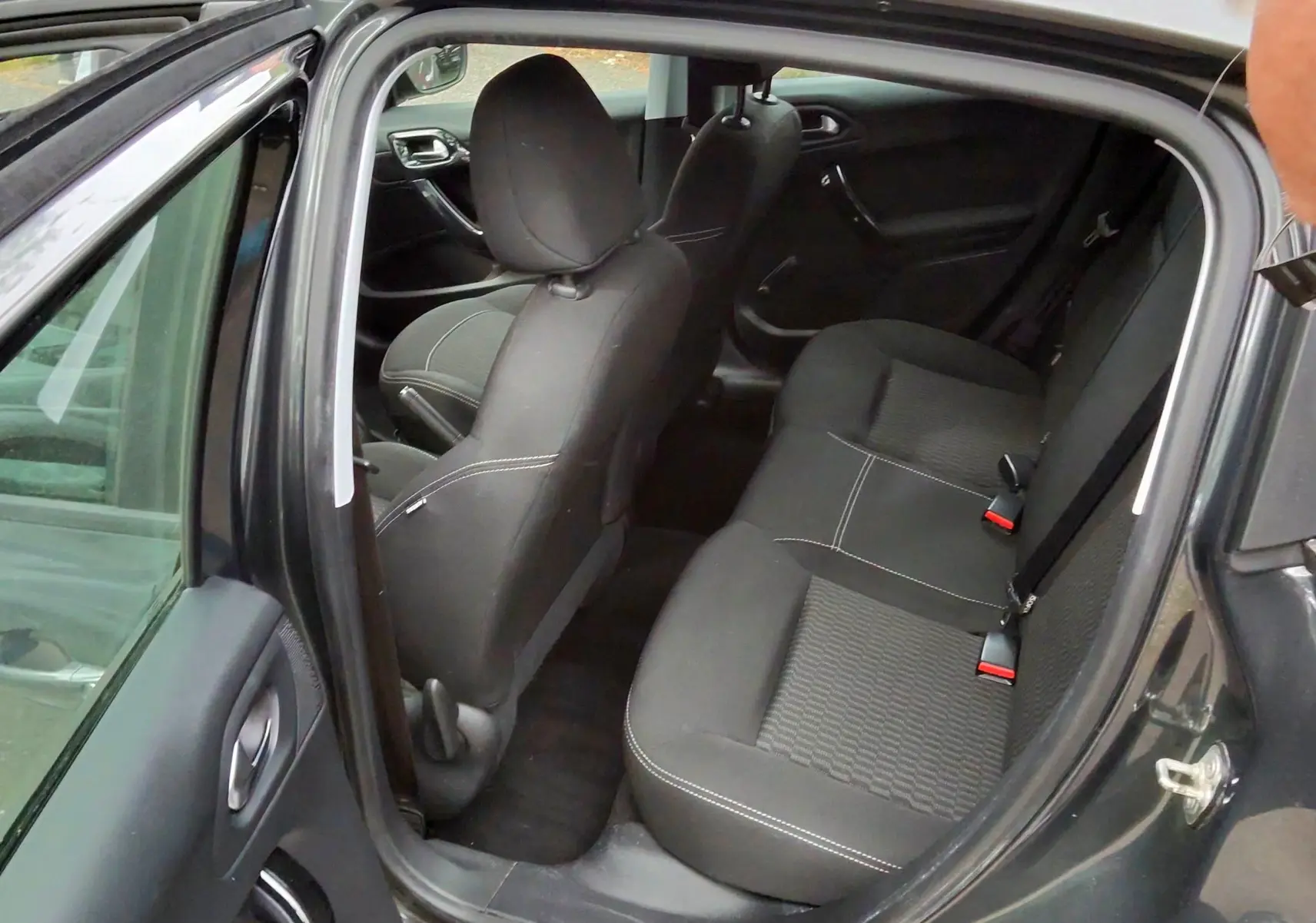 Vue intérieure côté gauche arrière d'une Peugeot 208 gris foncé métal, montrant les sièges arrière en tissu noir avec surpiqûres blanches.