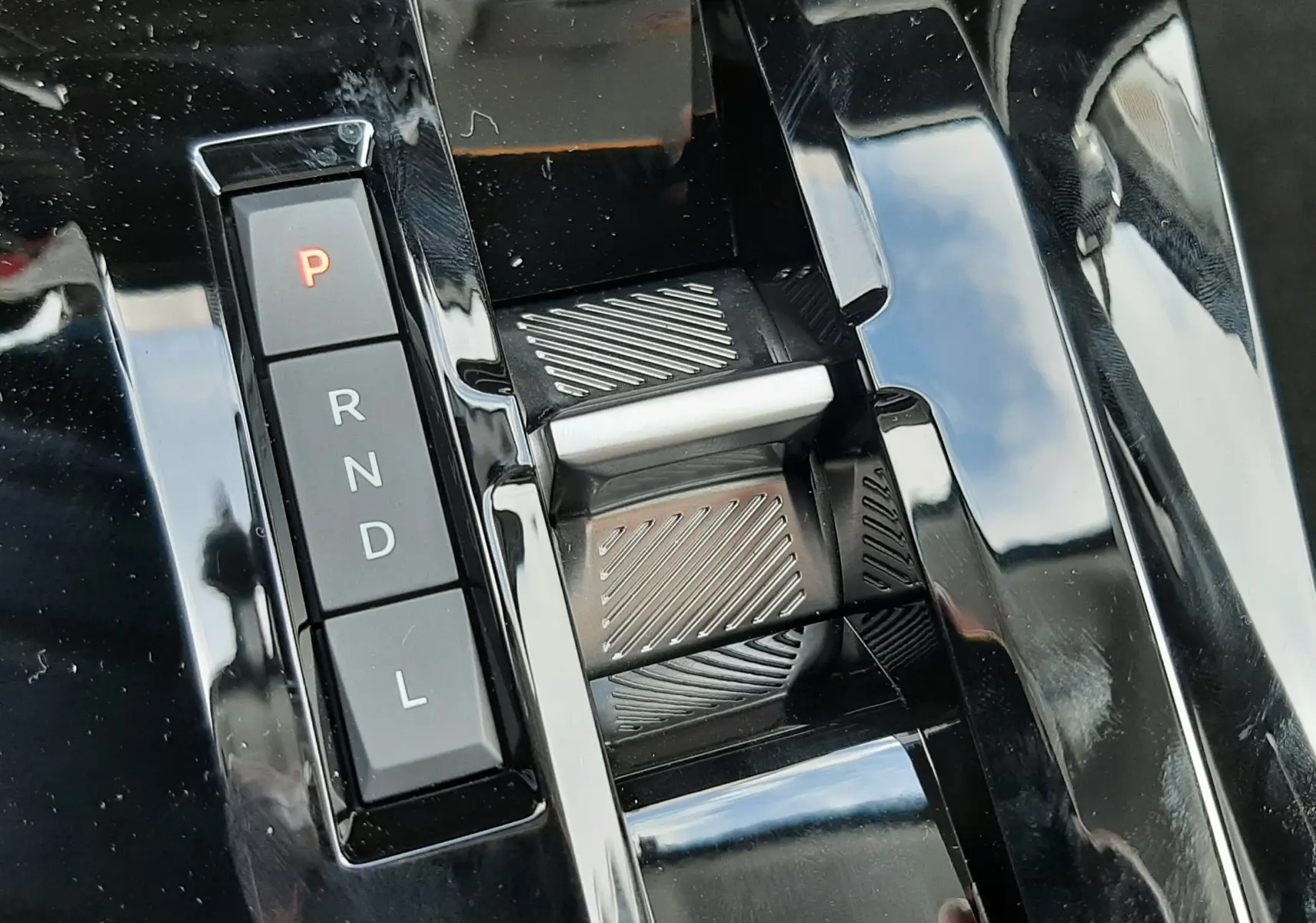 Gros plan sur la console centrale noire brillante avec sélecteur de boîte auto et boutons de mode de conduite.