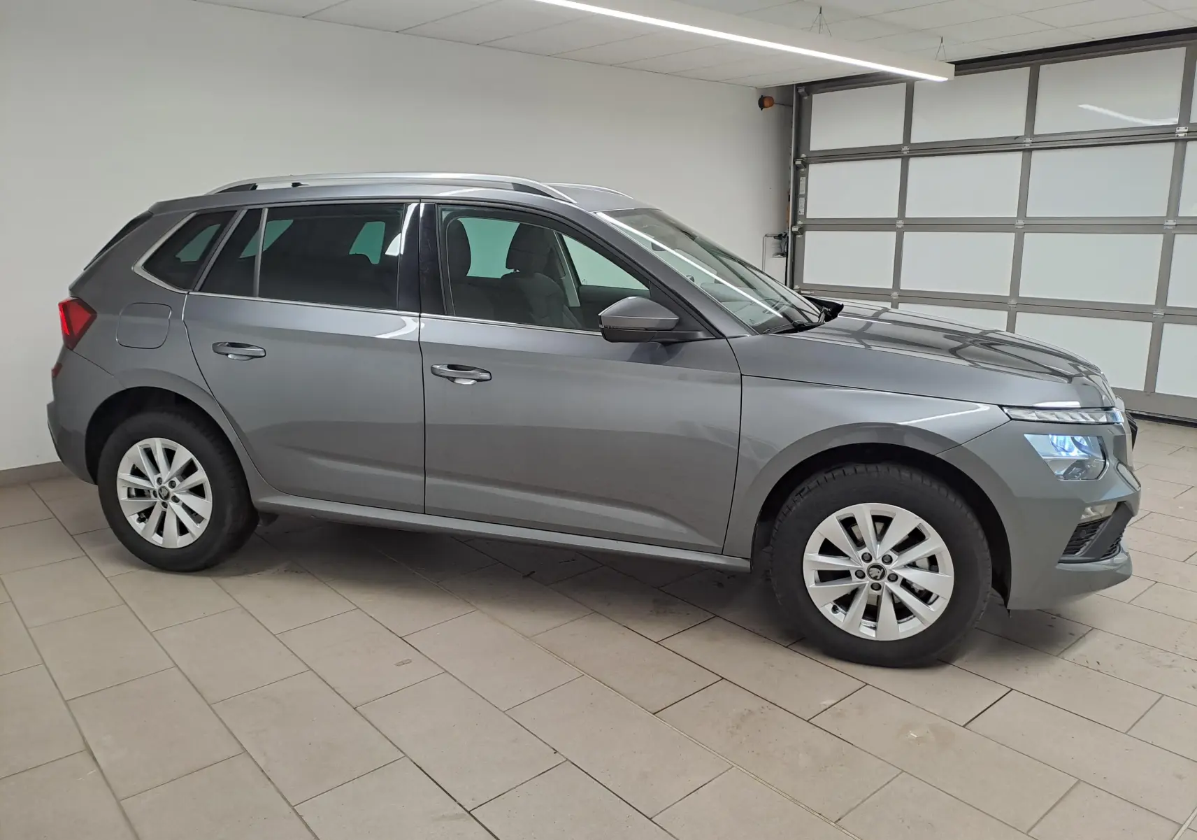 Vue de profil côté gauche d’un Skoda Kamiq gris graphite 2025 avec jantes alliage et caméra de recul visible.