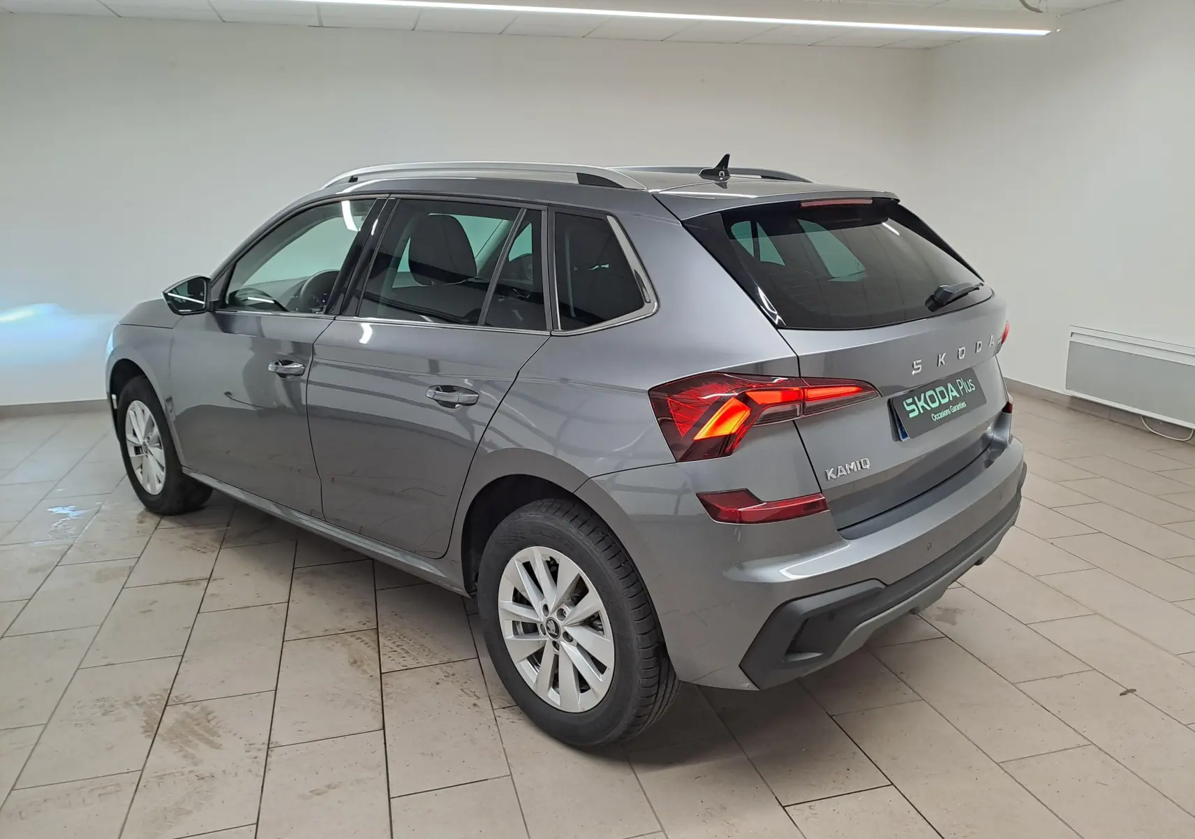 Vue 3/4 arrière droite du Skoda Kamiq 2025 gris graphite avec feux allumés et caméra de recul visible.