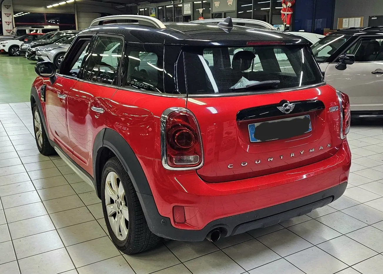 Vue 3/4 arrière droite d'une MINI Cooper Countryman rouge avec toit noir, en intérieur sur carrelage.
