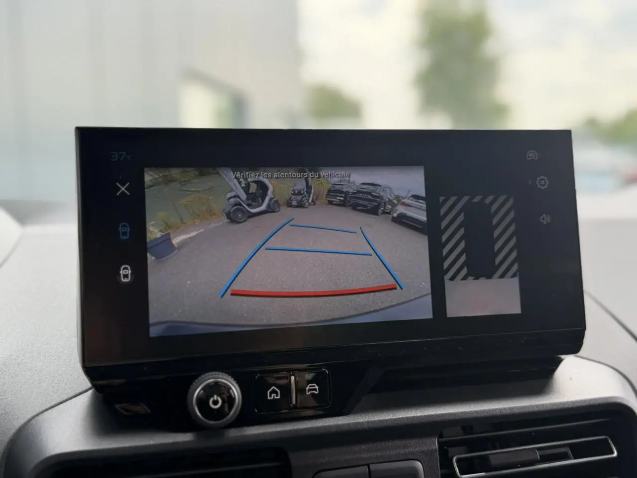 Écran tactile intérieur montrant la caméra de recul du Peugeot Rifter vert Sirkka en stationnement, vue arrière.