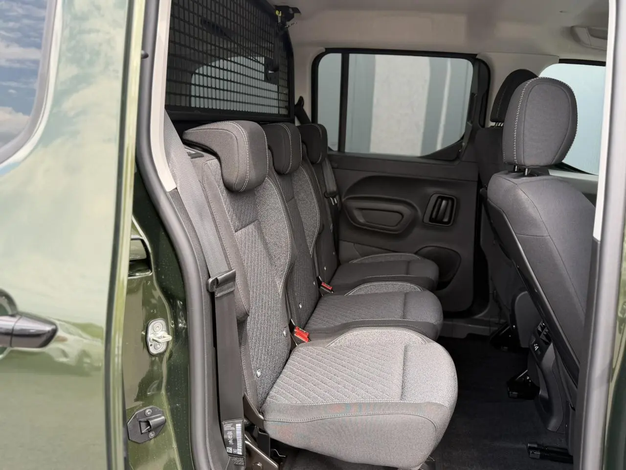 Vue latérale intérieure sur les trois sièges individuels arrière gris du Peugeot Rifter Vert Sirkka avec porte coulissante ouverte.