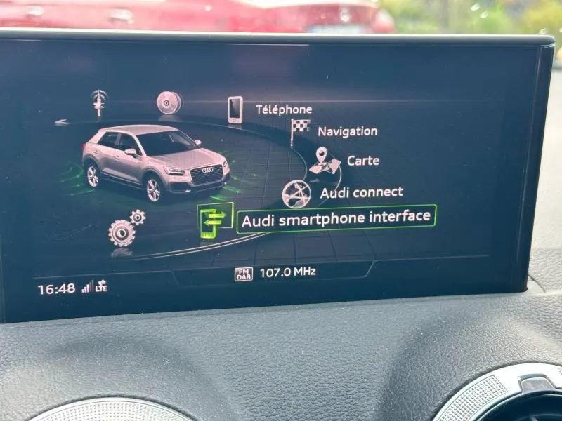 Écran multimédia affichant une Audi Q2 gris Daytona en vue 3/4 avant avec menu de navigation et connectivité smartphone.