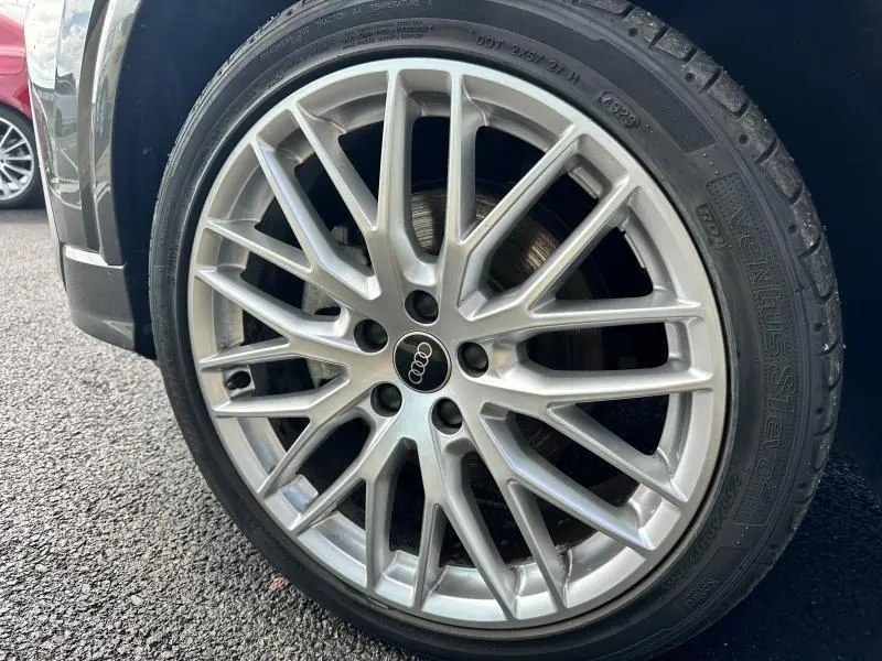 Gros plan sur la jante alu argentée à multiples branches de l'Audi Q2 gris Daytona nacré, roue avant côté gauche visible.