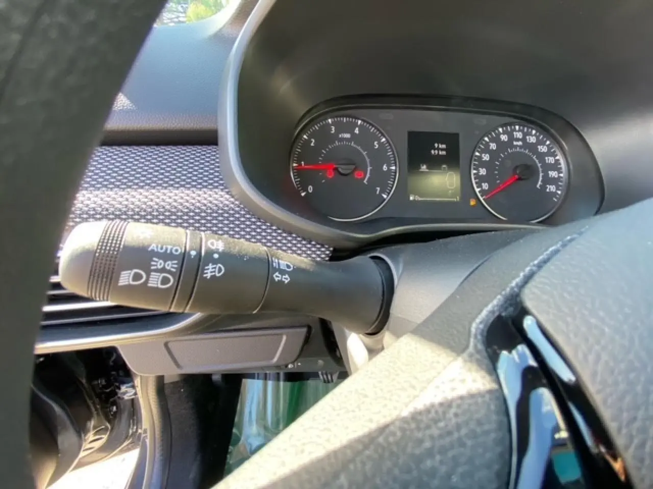 Gros plan sur le combiné d'instruments et la commande des phares à gauche du volant dans le tableau de bord gris de la Dacia Logan 2022.