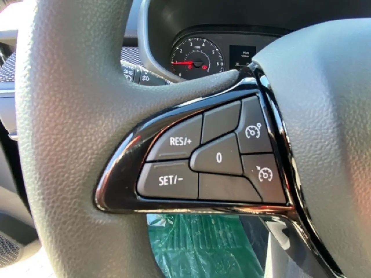 Gros plan sur les commandes du régulateur de vitesse au volant d'une Dacia Logan gris 2022, tableau de bord en arrière-plan.