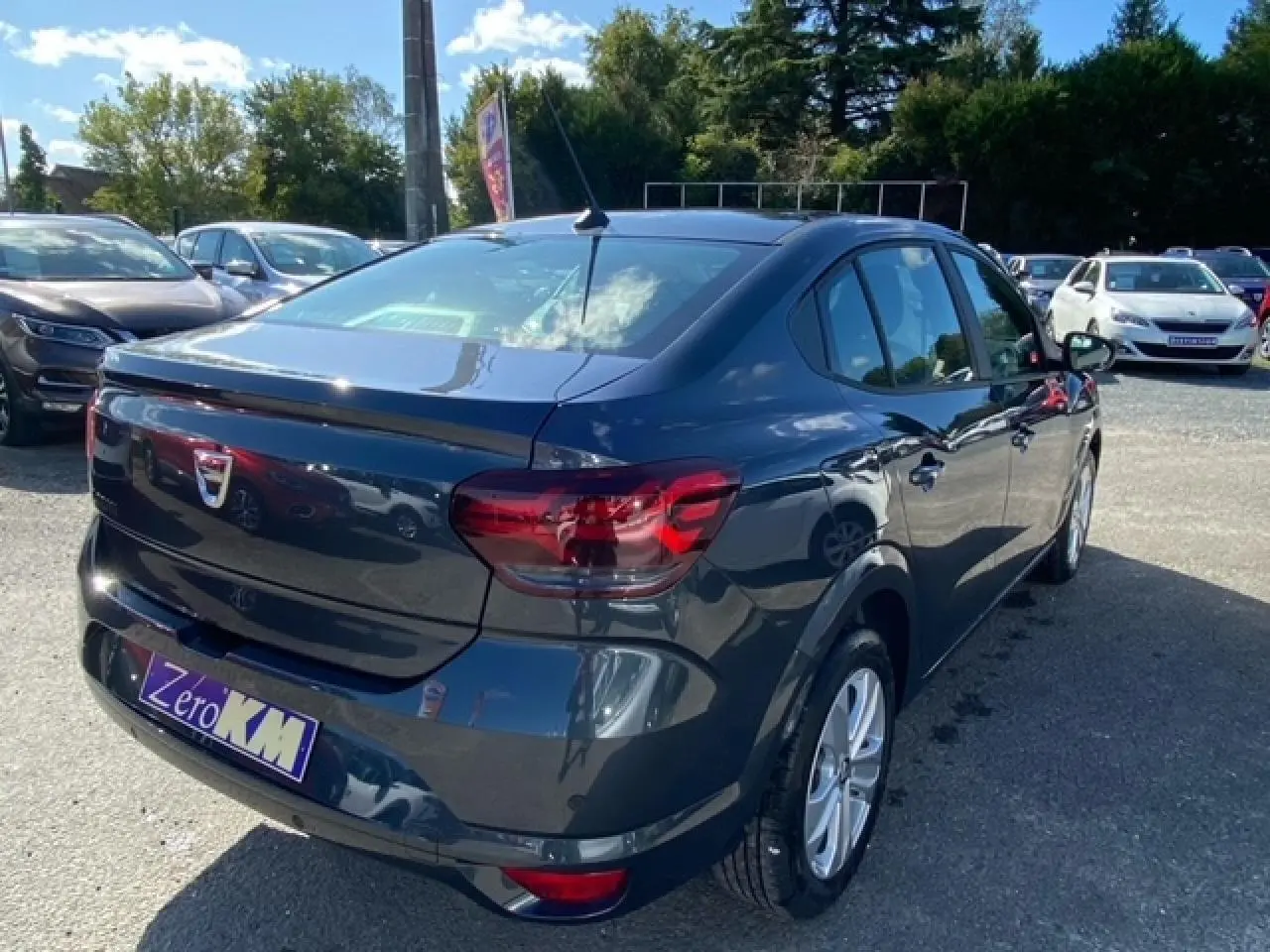 Vue 3/4 arrière droite d'une Dacia Logan gris métallisé 2022 avec feux arrière rouges et antenne de toit visible.