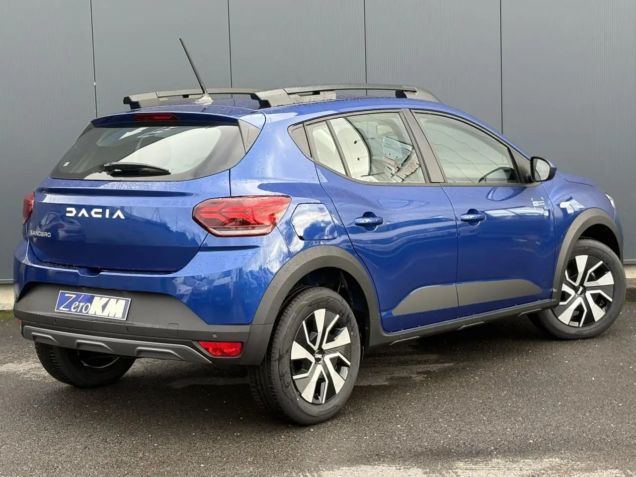 Vue 3/4 arrière droite d'une Dacia Sandero Stepway 2025 Bleu Iron avec barres de toit et jantes spécifiques.