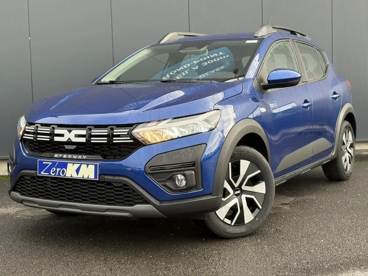 Dacia Sandero Stepway TCE 90 bleu Iron en 3/4 avant droit, avec barres de toit et jantes spécifiques Atara Dark.