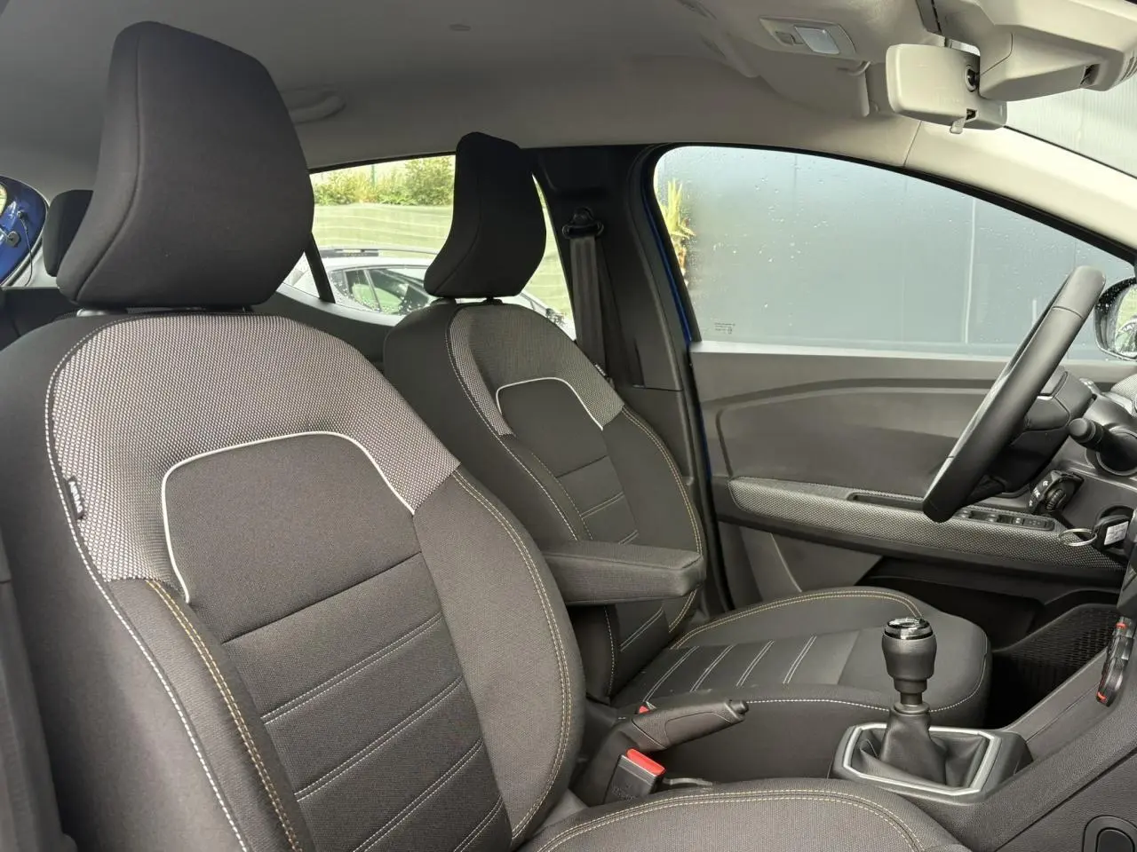 Vue intérieure côté droit de la Dacia Sandero Stepway 2025 Bleu Iron, sièges tissu avec accoudoir et volant Soft Feel.