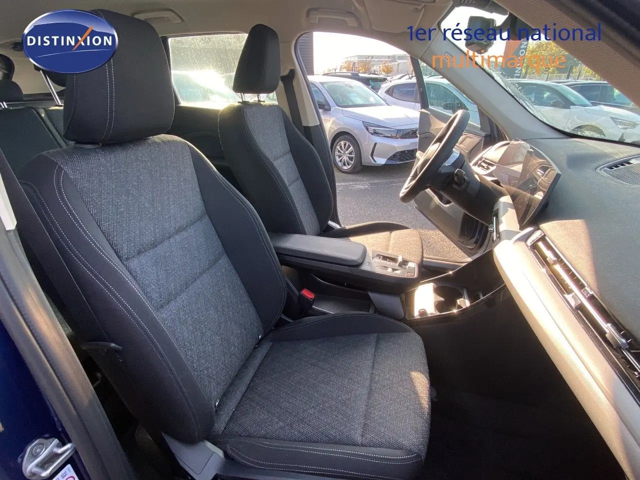 Vue intérieure côté conducteur du BMW X1 18I 136CH avec sièges tissu gris noir et tableau de bord moderne.