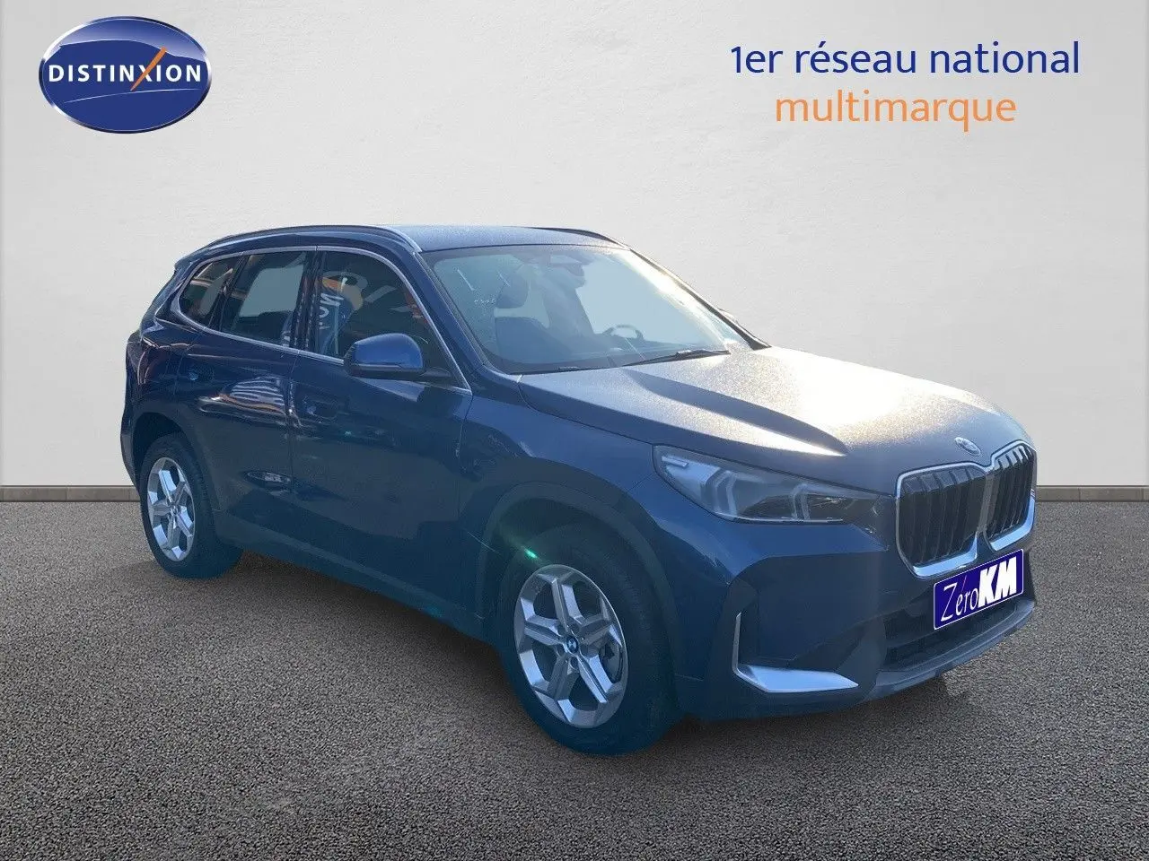 BMW X1 18I bleu Phytonic Metal en 3/4 avant droit, avec calandre imposante et jantes argentées.