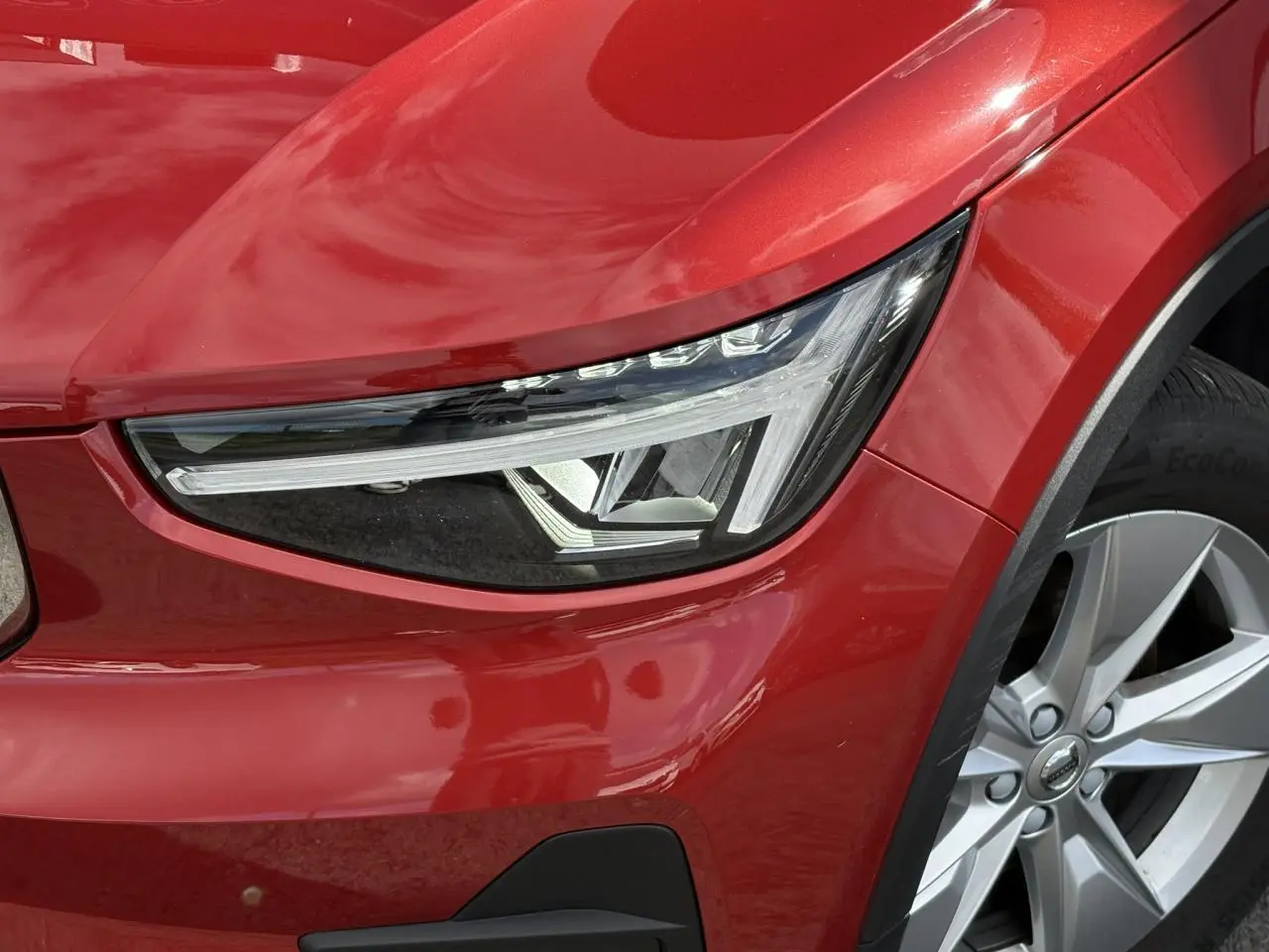 Gros plan sur le phare avant gauche et la roue alliage 18'' du Volvo XC40 rouge Fusion 2024.