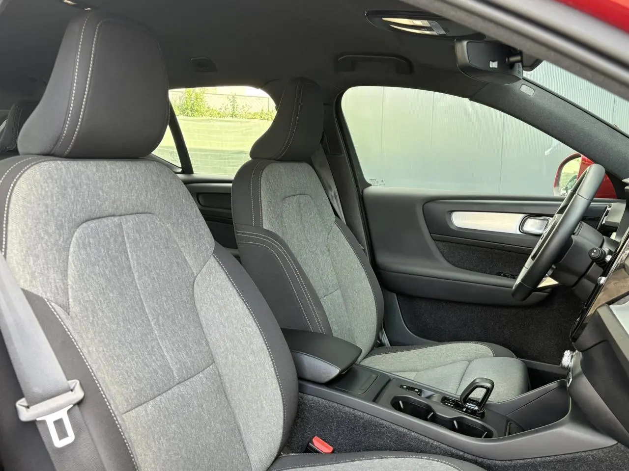 Vue intérieure côté conducteur du Volvo XC40 rouge Fusion, mettant en valeur les sièges gris clair et la console centrale moderne.