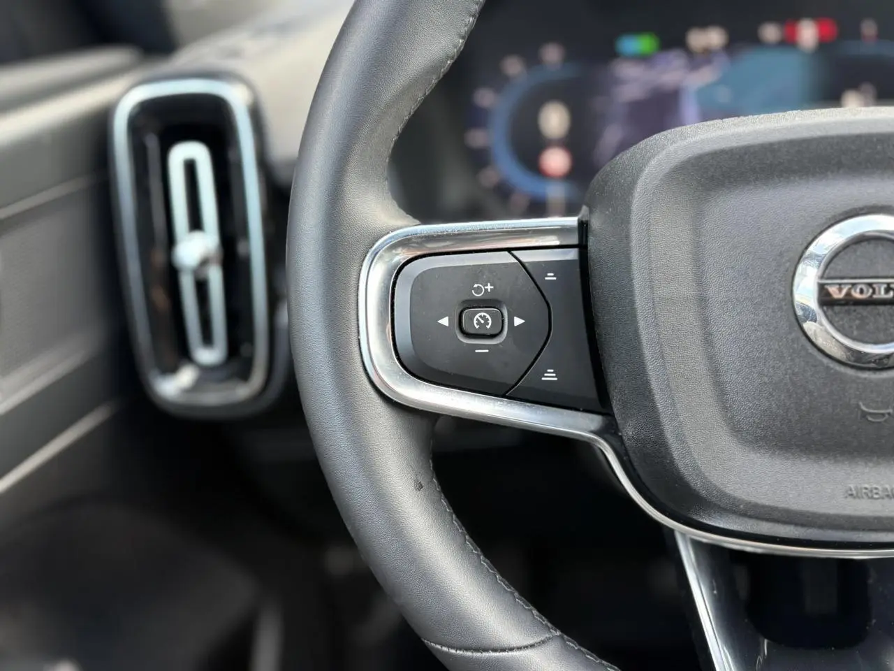 Gros plan sur la partie gauche du volant noir du Volvo XC40 2024 avec commandes de régulateur et aérateur vertical.