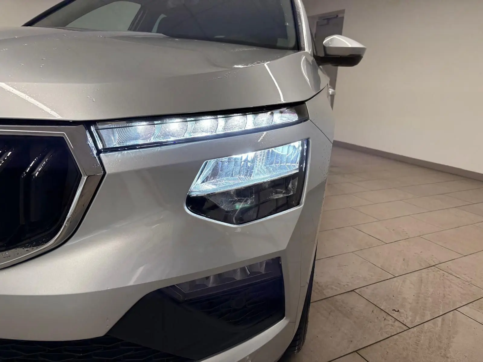 Gros plan sur le phare avant droit allumé du Skoda Kamiq gris argent, mettant en valeur les lignes modernes du SUV.