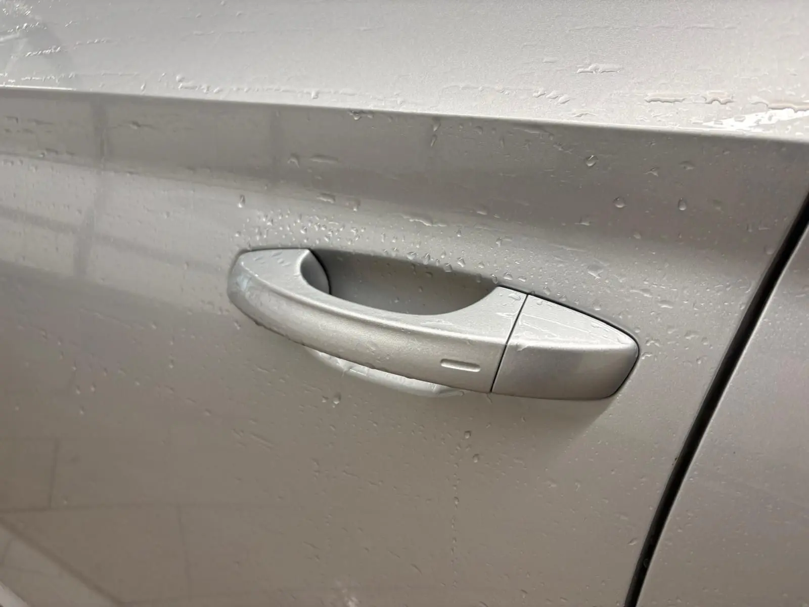 Poignée de porte côté gauche gris argent métallisé du Skoda Kamiq 2025 avec gouttes d'eau visibles.