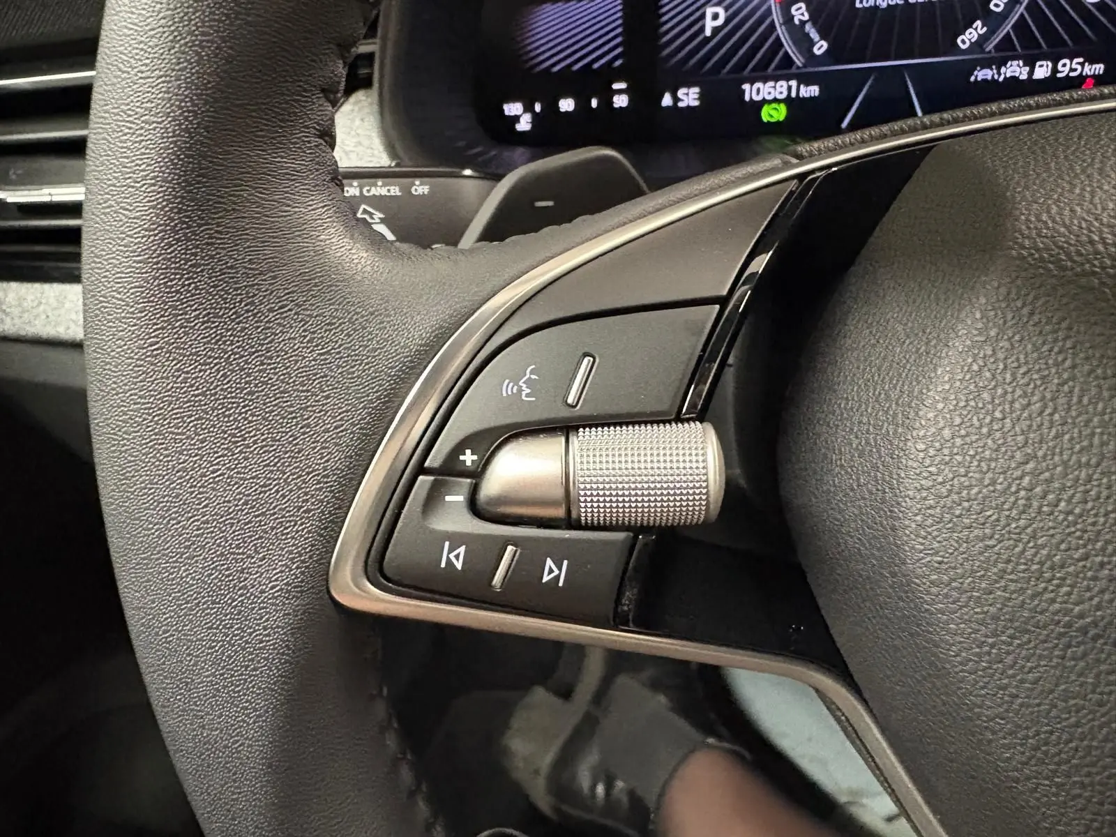 Gros plan sur les commandes gauche du volant noir du Skoda Kamiq gris argent, avec affichage numérique en arrière-plan.