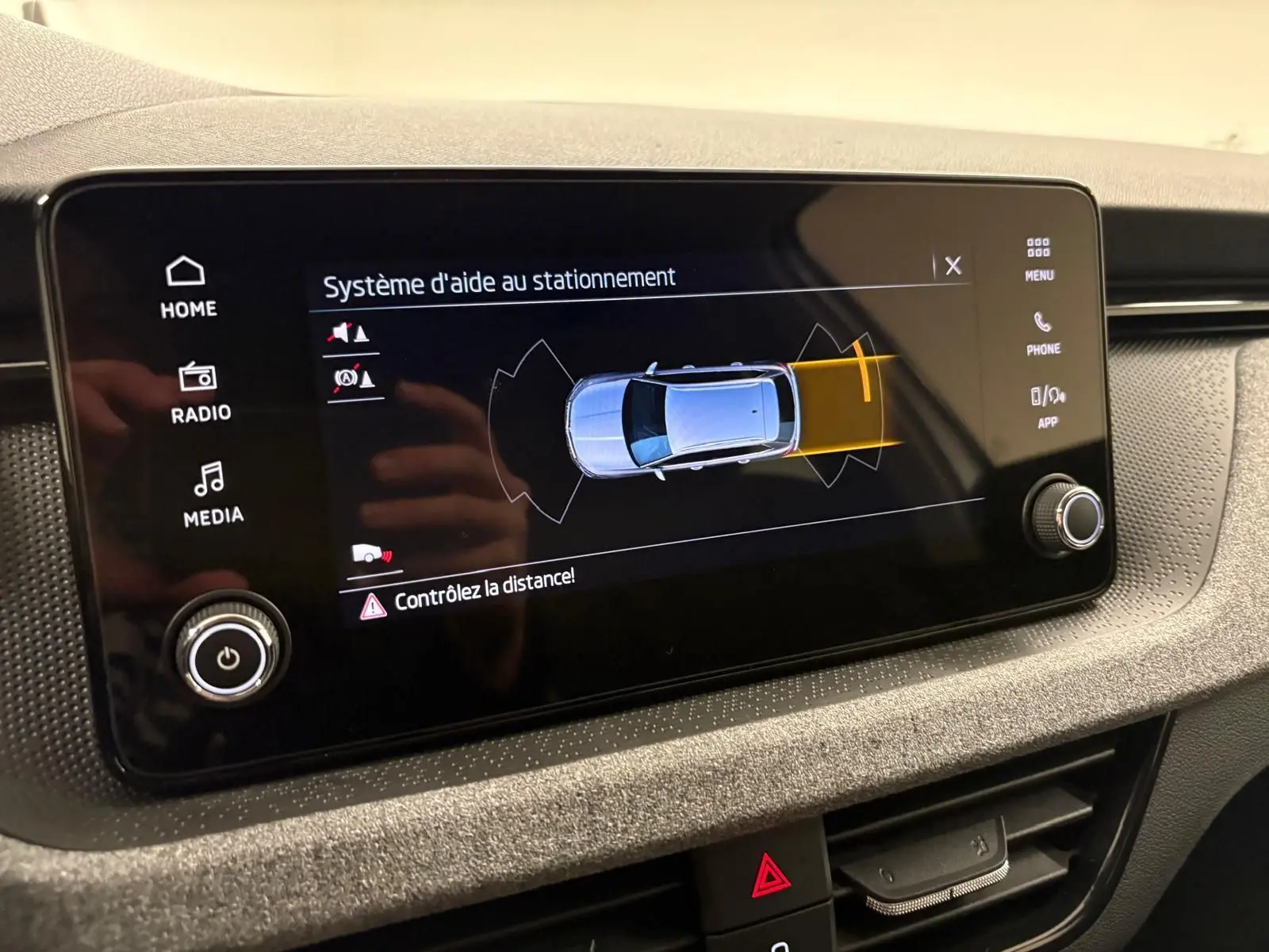 Écran central montrant l’aide au stationnement avec vue du dessus d’un Skoda Kamiq gris argent en alerte arrière.