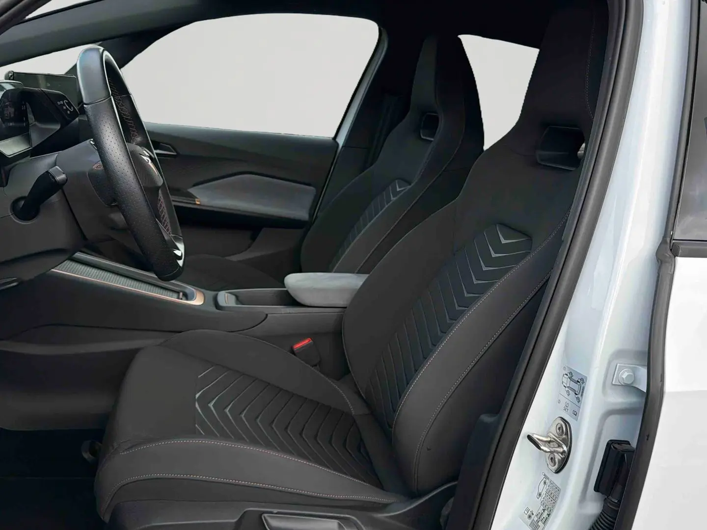 Vue intérieure côté conducteur de la CUPRA Born blanche 2024, sièges sport noirs avec surpiqûres et volant multifonction.