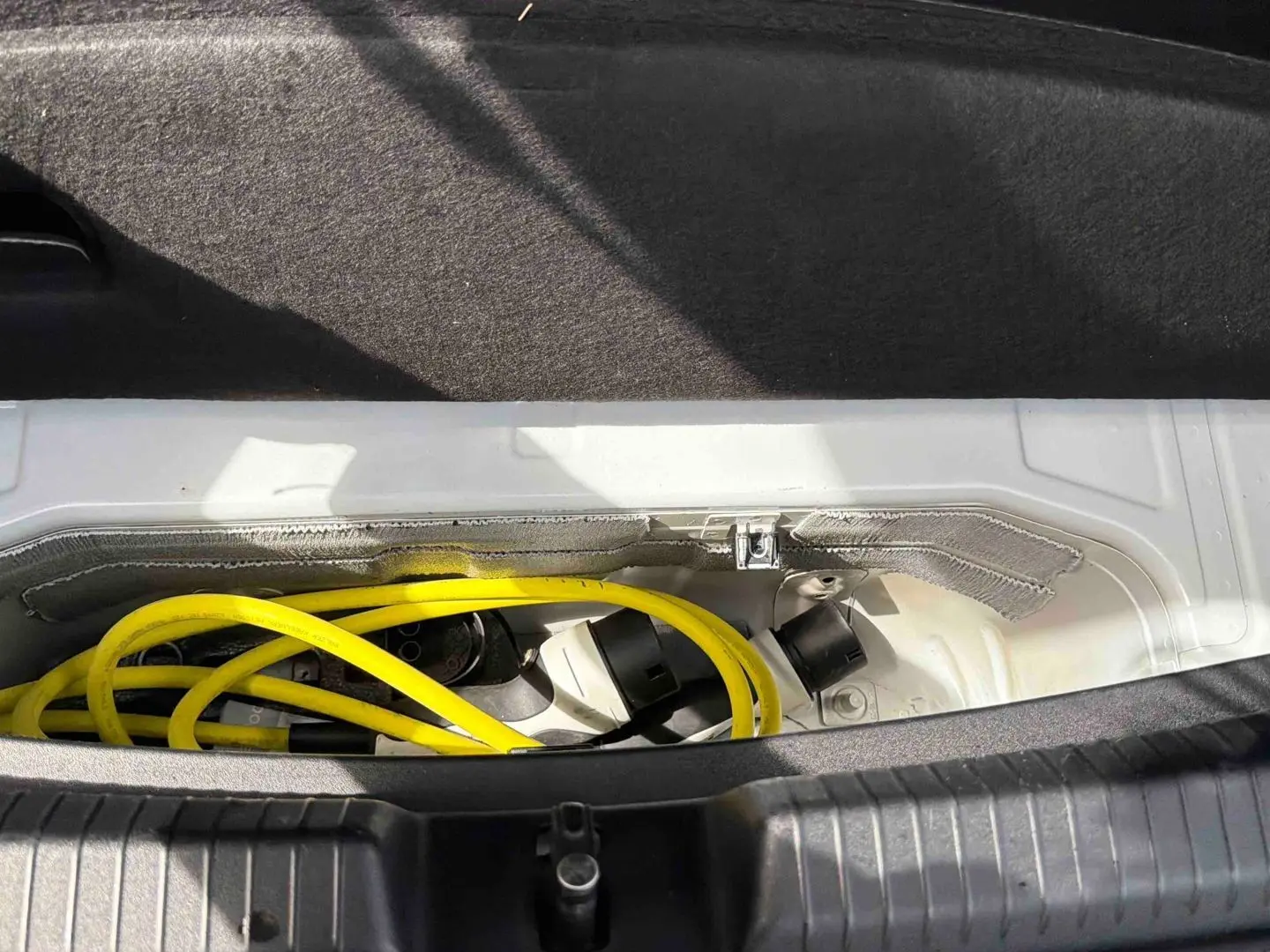 Coffre ouvert montrant le câble de recharge jaune du CUPRA Born e-boost blanc, vue rapprochée intérieure arrière.
