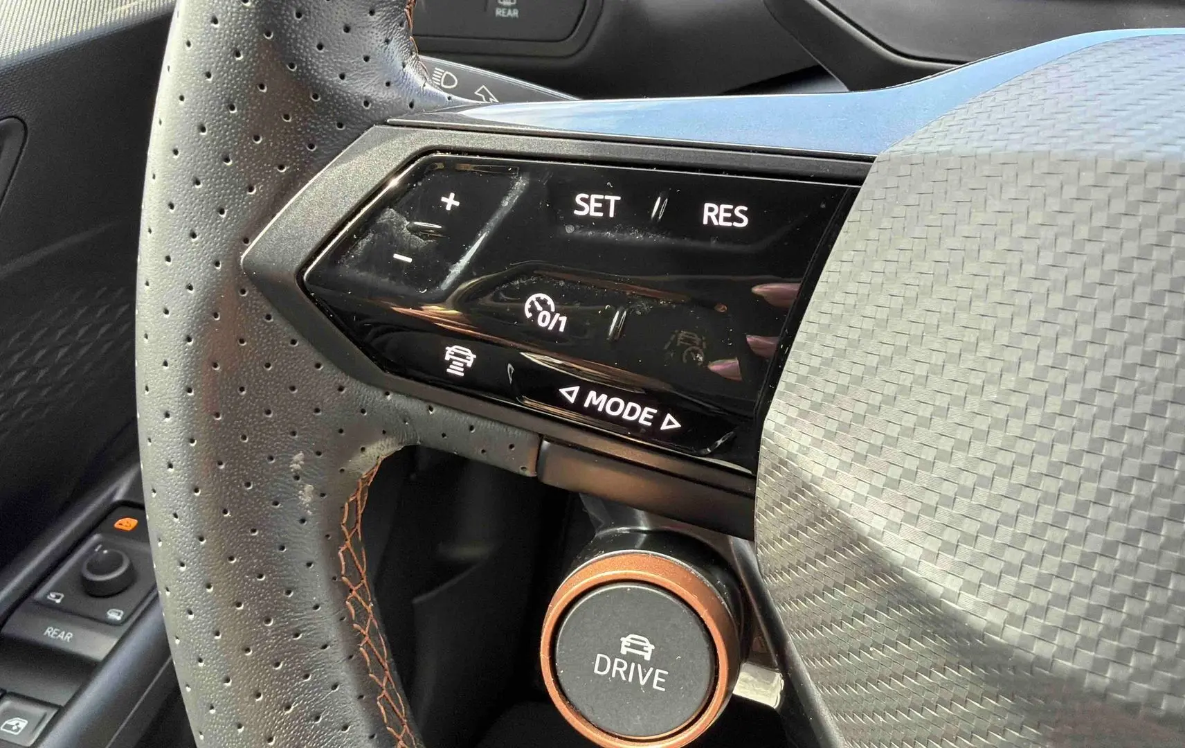 Gros plan sur le volant perforé noir de la CUPRA Born 2024 avec commandes de régulateur et bouton Drive orange.