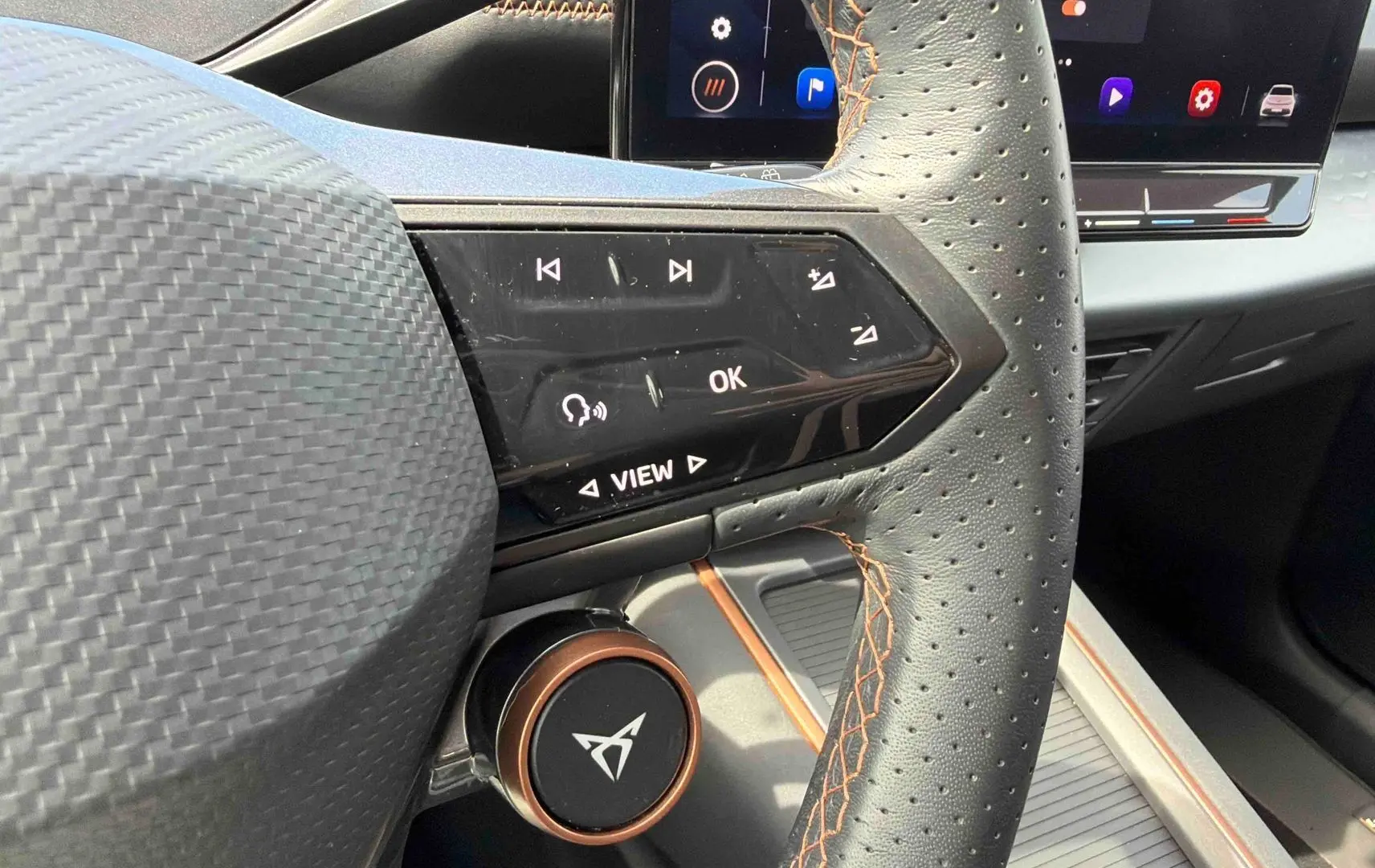 Gros plan sur le volant perforé noir avec surpiqûres cuivre du CUPRA Born 2024 et commandes multifonctions côté gauche.