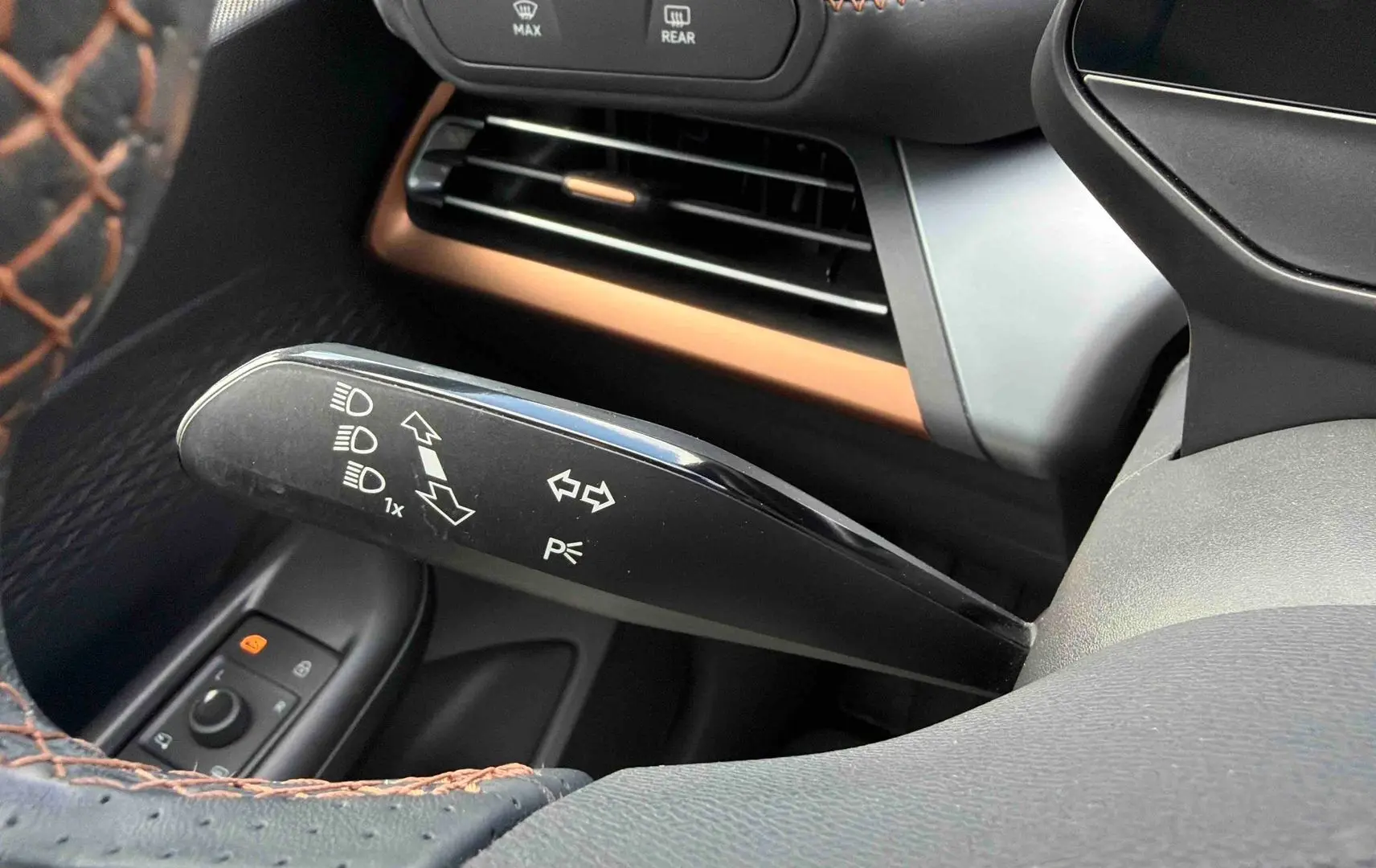 Gros plan sur la manette de clignotant noire à gauche du volant, avec coutures marron visibles sur le volant du CUPRA Born blanc.