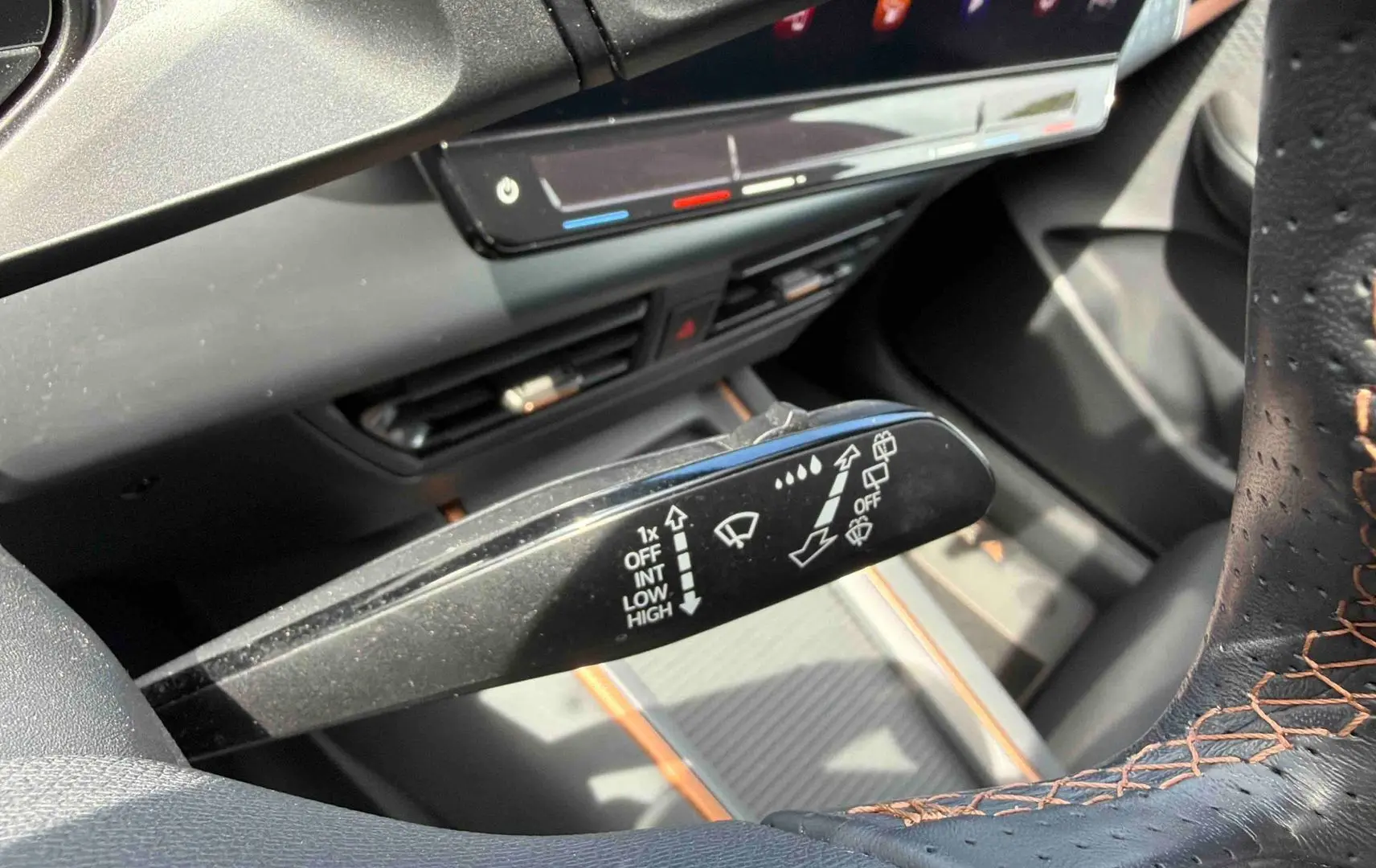 Gros plan sur la commande d’essuie-glace à gauche du volant perforé noir avec surpiqûres orange dans un CUPRA Born blanc.
