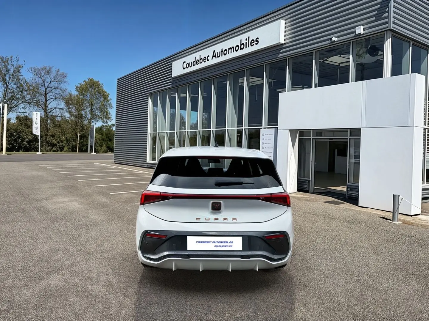 Vue arrière d'une CUPRA Born blanche 2024 avec feux LED et bandeau lumineux Infinite Light, stationnée devant un showroom.