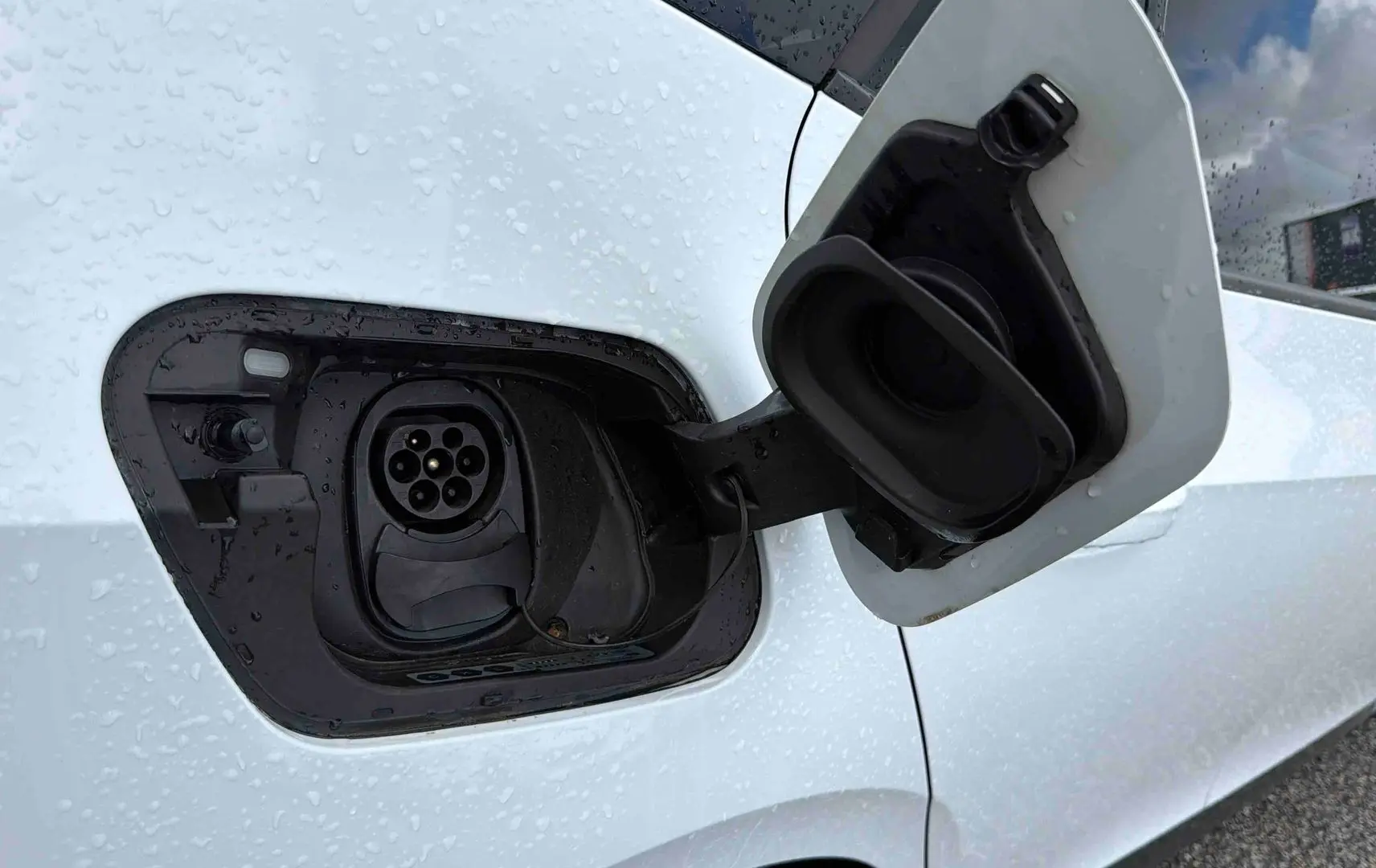 Prise de recharge électrique ouverte sur le côté gauche d'une CUPRA Born blanche sous la pluie.