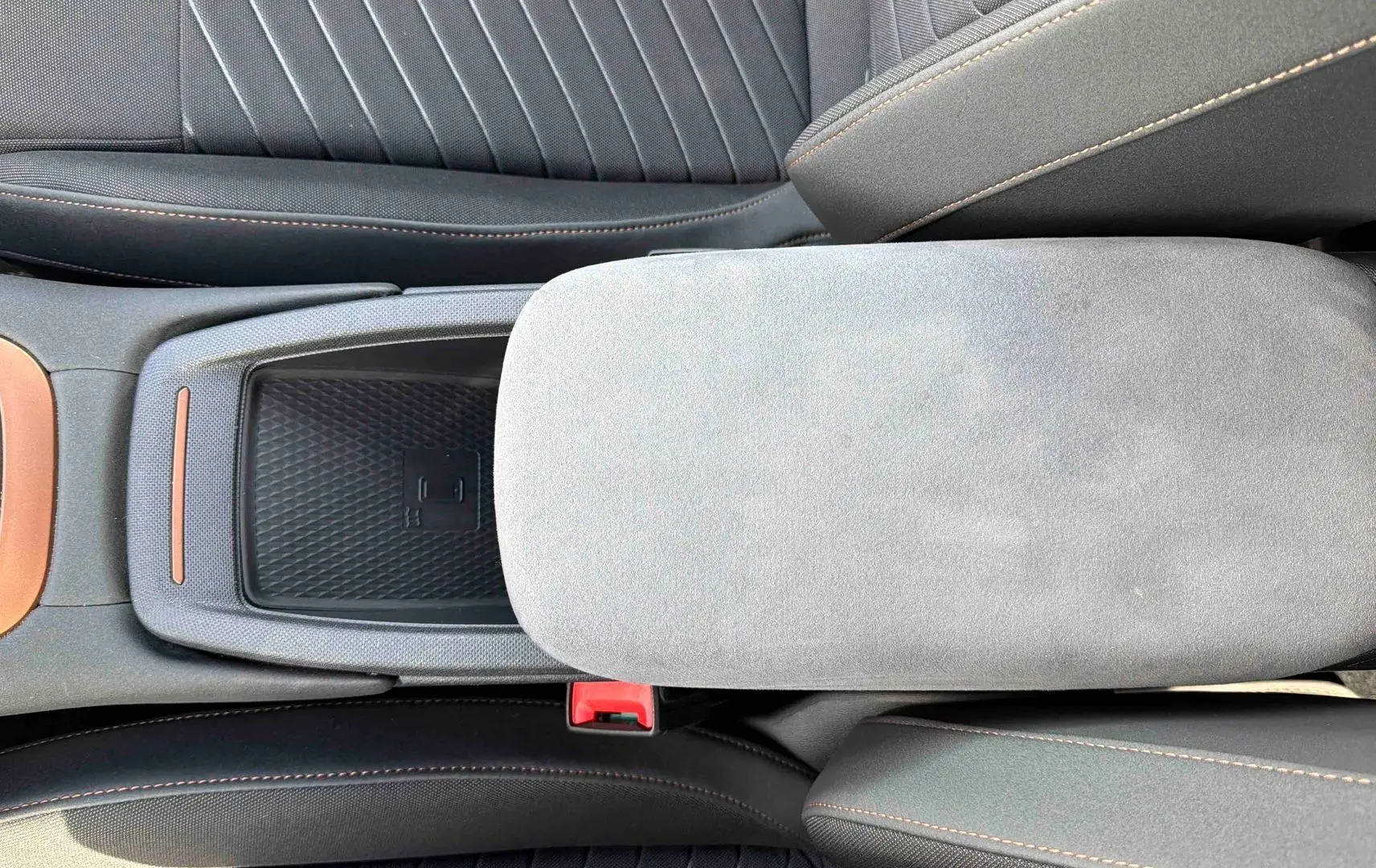 Vue plongeante sur la console centrale du CUPRA Born 2024, avec accoudoir gris clair et sellerie noire à surpiqûres cuivrées.