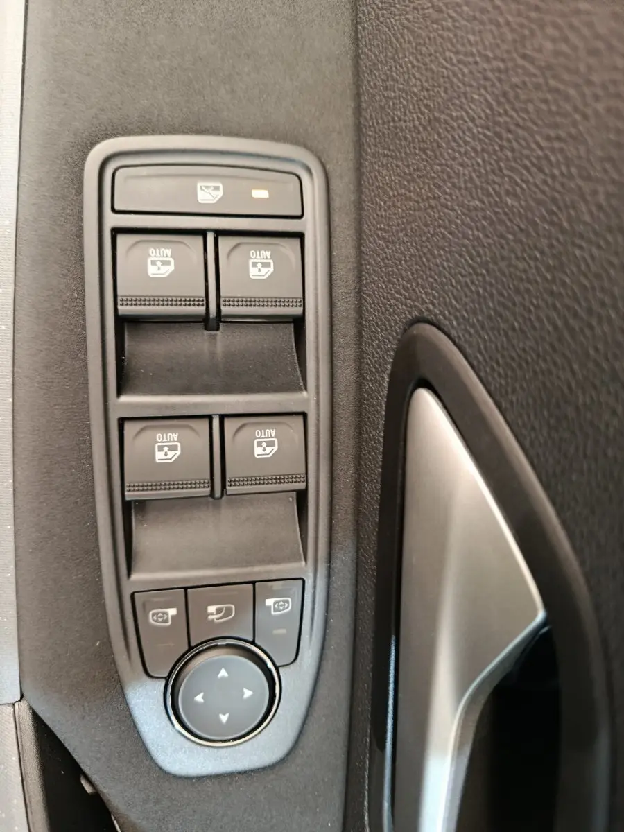 Gros plan sur les commandes des vitres électriques et réglages des rétroviseurs côté conducteur du Dacia Duster noir 2026.