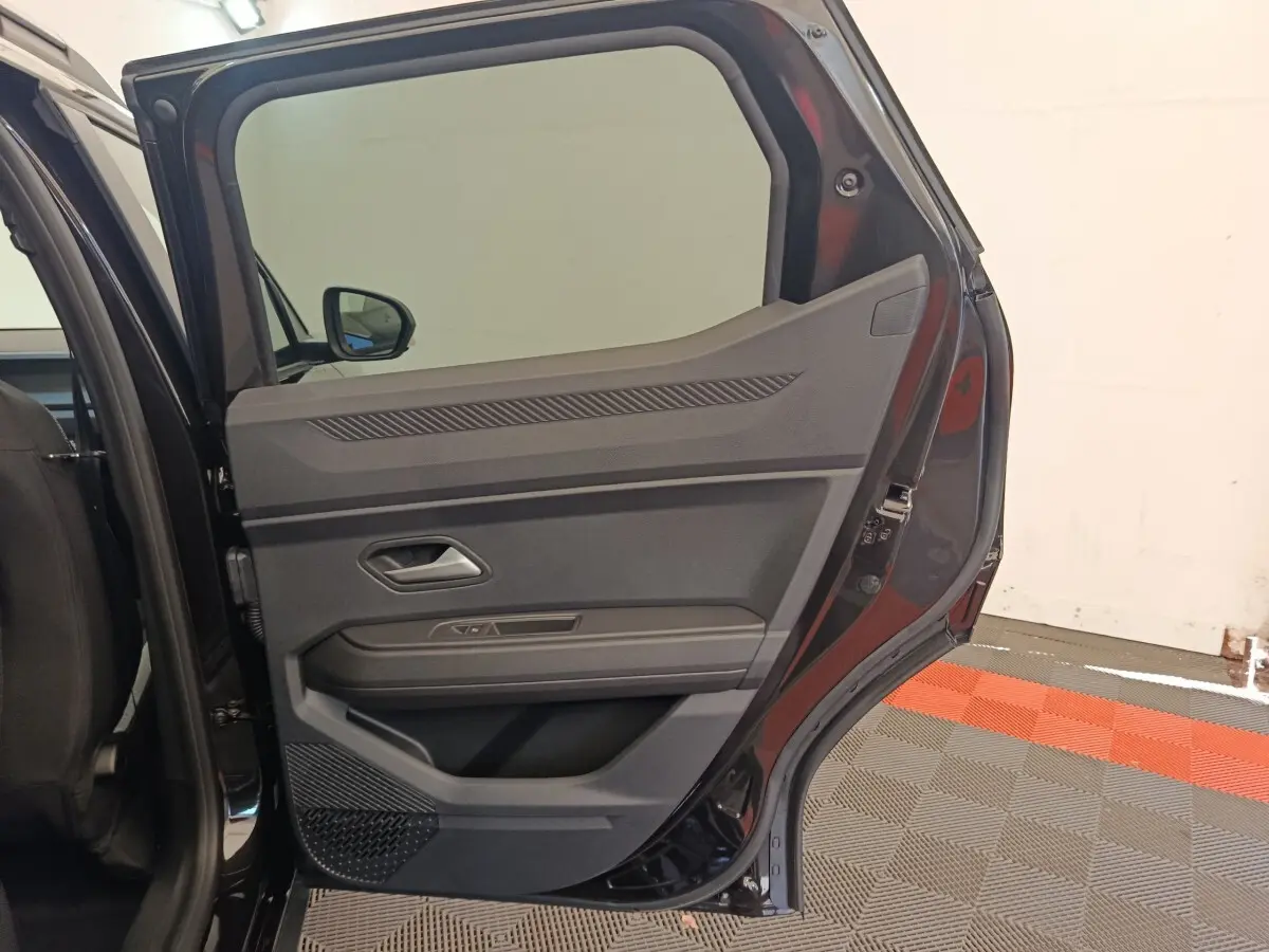 Vue intérieure de la porte arrière droite noire du Dacia Duster Journey Hybrid 155 avec détails des commandes et rangement.