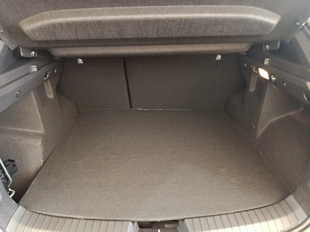 Vue intérieure du coffre noir du Dacia Duster Journey Hybrid 155, montrant l'espace de chargement avec tapis et éclairage latéral.