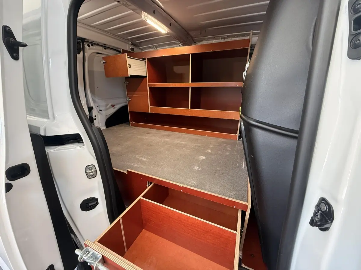 Vue intérieure côté gauche du Citroën Berlingo blanc 2019, montrant un aménagement bois avec étagères et tiroir ouvert.