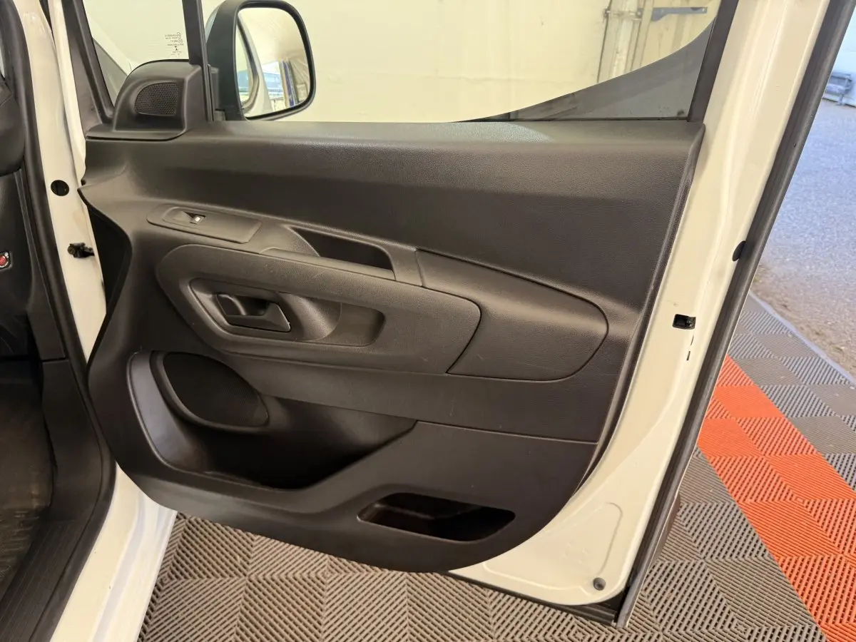 Vue rapprochée de la porte avant gauche blanche d’un Citroën Berlingo 2019, intérieur noir avec poignée et commande de vitre.