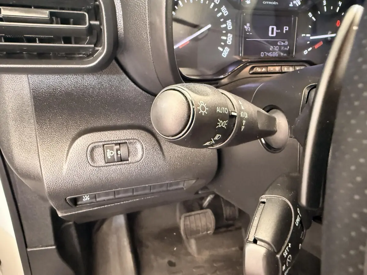 Gros plan sur la commande des phares et le tableau de bord noir du Citroën Berlingo blanc, vue côté conducteur.