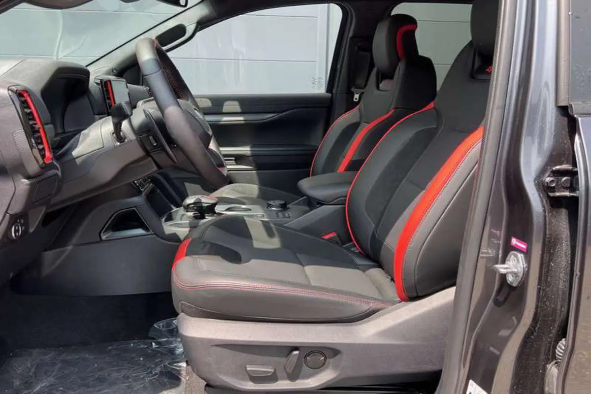 Intérieur du Ford Ranger Raptor 2025 en gris météore, vue côté gauche sur les sièges noirs avec surpiqûres rouges sportives.