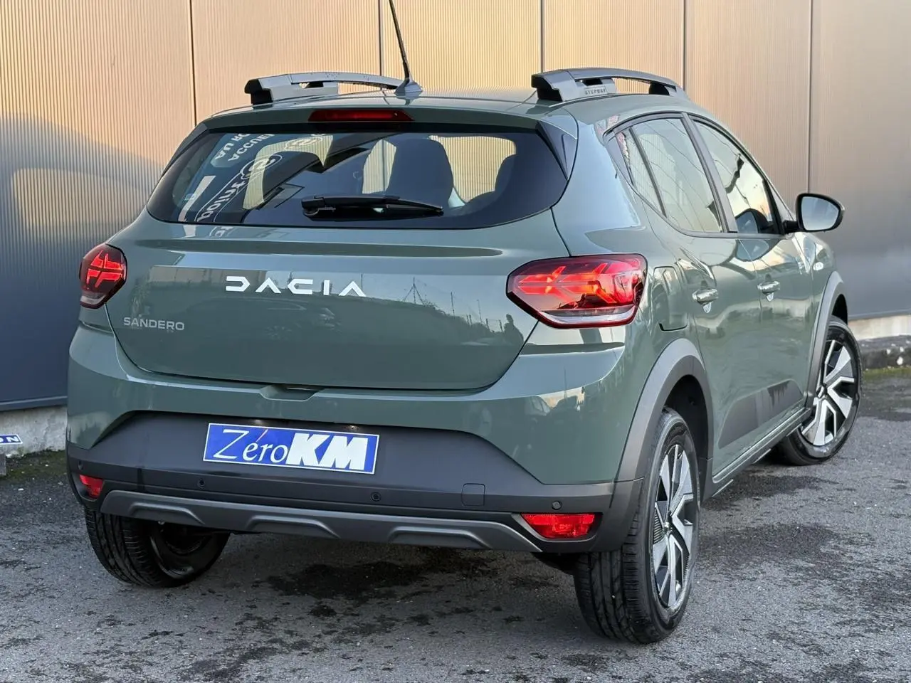Vue 3/4 arrière droite d'une Dacia Sandero Stepway 2025 en kaki lichen avec barres de toit et feux arrière LED en Y.